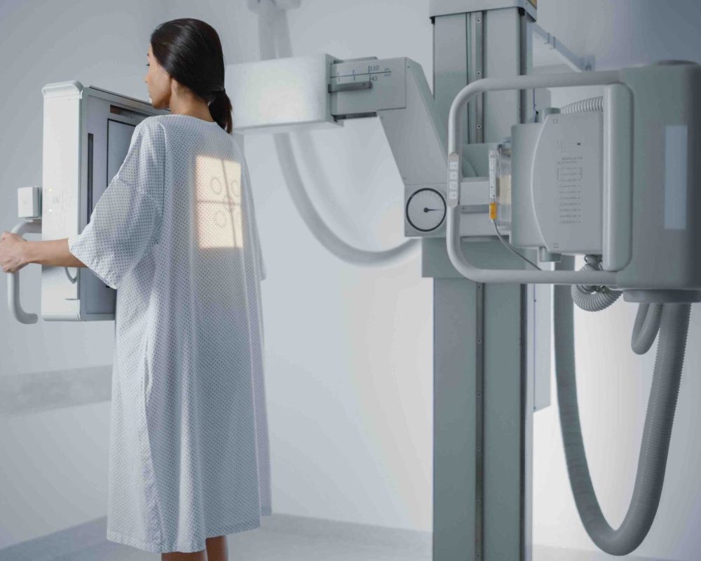 Hospital,Radiology,Room:,Beautiful,Multiethnic,Woman,Standing,In,Medical,Gown Hospital Radiology Room: Beautiful Multiethnic Woman Standing in Medical Gown in the X-Ray Machine. Adult Female Undergoes Healthcare Exam and is Scanning Chest, Heart, Lungs in Modern Clinic Office.